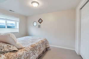 Bedroom featuring a textured ceiling, visible vents, baseboards, and light carpet