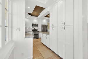 Kitchen featuring tasteful backsplash, crown molding, light tile patterned flooring, white cabinetry, and appliances with stainless steel finishes