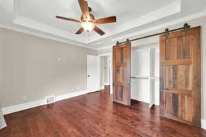 Unfurnished bedroom with visible vents, dark wood-type flooring, a raised ceiling, and a barn door