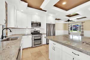 Kitchen with ornamental molding, appliances with stainless steel finishes, a sink, and white cabinets
