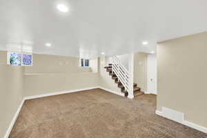 Basement with carpet floors, visible vents, baseboards, and stairway