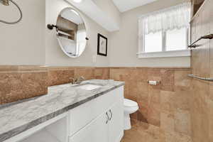 Full bathroom featuring a tile shower, toilet, vanity, tile walls, and wainscoting