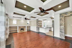 Unfurnished living room featuring a fireplace with flush hearth, crown molding, ceiling fan, and coffered ceiling