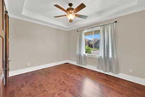 Spare room with a tray ceiling, crown molding, dark wood-type flooring, and a ceiling fan