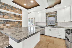 Kitchen with a sink, wood ceiling, a tray ceiling, white cabinets, and appliances with stainless steel finishes
