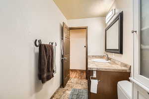 Half bathroom featuring toilet, vanity, stone finish flooring, baseboards, and a textured ceiling