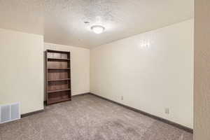 Carpeted empty room with baseboards, a textured wall, a textured ceiling, and visible vents