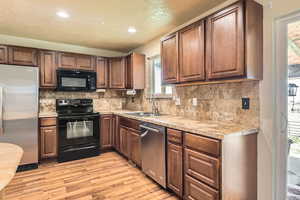 Kitchen featuring a sink, black appliances, a wealth of natural light, light wood finished floors, and recessed lighting