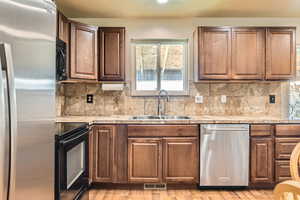 Kitchen featuring tasteful backsplash, a sink, black appliances, light wood finished floors, and visible vents