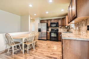 Kitchen with a sink, light wood-type flooring, backsplash, tile countertops, and black appliances
