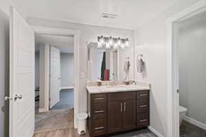 Bathroom with toilet, wood finished floors, vanity, baseboards, and visible vents