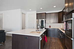 Kitchen featuring dark wood-style flooring, dark brown cabinets, recessed lighting, light countertops, and appliances with stainless steel finishes