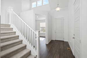Entryway with a high ceiling, a wealth of natural light, stairs, and dark wood-style flooring
