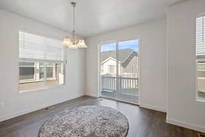 Unfurnished dining area with an inviting chandelier, dark wood-style flooring, visible vents, and baseboards