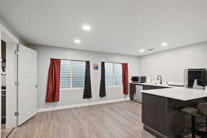 Kitchen with light wood finished floors, stainless steel dishwasher, recessed lighting, light countertops, and a breakfast bar area