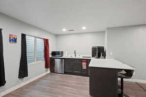 Kitchen featuring stainless steel appliances, a peninsula, a sink, a kitchen bar, and light countertops