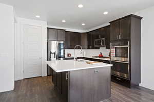 Kitchen with appliances with stainless steel finishes, dark brown cabinets, dark wood-style floors, and recessed lighting