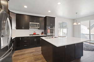 Kitchen with hanging light fixtures, an island with sink, light countertops, appliances with stainless steel finishes, and recessed lighting