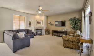 Living area featuring a tiled fireplace, carpet flooring, and ceiling fan