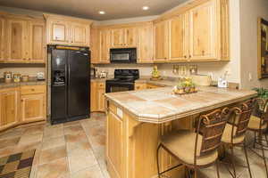 Kitchen featuring recessed lighting, tile countertops, a breakfast bar area, and black appliances