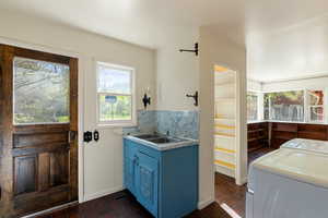 Clothes washing area with washing machine and clothes dryer, a wealth of natural light, dark tile patterned flooring, and a sink