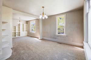 Carpeted empty room featuring visible vents, a wealth of natural light, and an inviting chandelier