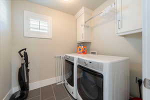 Clothes washing area featuring cabinet space, baseboards, washer and dryer, and dark tile patterned flooring