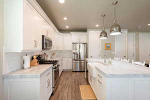 Kitchen with recessed lighting, backsplash, a kitchen island with sink, appliances with stainless steel finishes, and white cabinetry