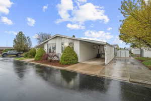 View of front of property with entry steps, concrete driveway, an outbuilding, a carport, and a storage unit