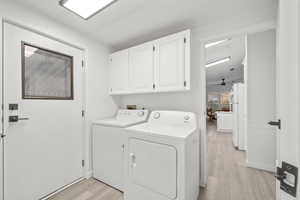 Laundry area featuring light wood-type flooring, separate washer and dryer, and cabinet space