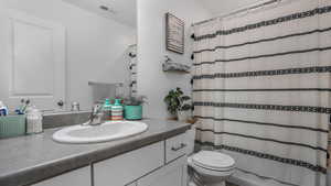 Full bath with toilet, vanity, visible vents, and a shower with curtain