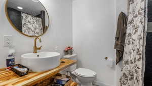 Full bathroom featuring a sink, toilet, a shower with shower curtain, and baseboards