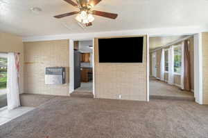 Unfurnished living room featuring brick wall, heating unit, and carpet