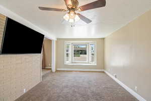 Unfurnished living room with brick wall, carpet floors, a ceiling fan, and a textured ceiling