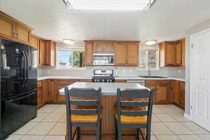 Kitchen featuring brown cabinetry, appliances with stainless steel finishes, light tile patterned floors, and a sink