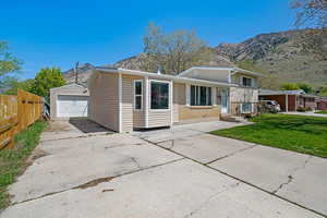 Tri-level home featuring a mountain view, a detached garage, concrete driveway, fence, and an outdoor structure