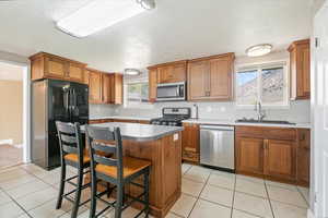 Kitchen featuring brown cabinetry, a sink, a textured ceiling, and appliances with stainless steel finishes