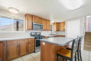 Kitchen featuring a sink, a textured ceiling, brown cabinetry, light tile patterned floors, and appliances with stainless steel finishes