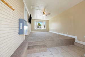 Carpeted empty room with brick wall, baseboards, tile patterned flooring, and ceiling fan
