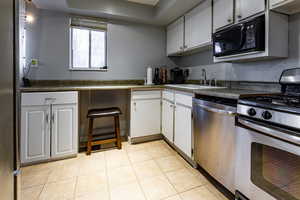 Kitchen featuring dark countertops, a sink, light tile patterned floors, stainless steel appliances, and white cabinets