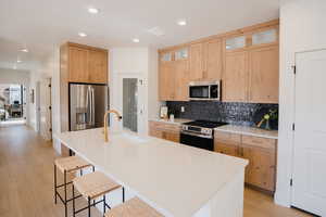 Model Home PicsKitchen with stainless steel appliances, light brown cabinetry, a sink, a kitchen bar, and decorative backsplash