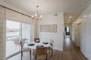 Model Home PicsDining space featuring wood finished floors, visible vents, a notable chandelier, and a healthy amount of sunlight