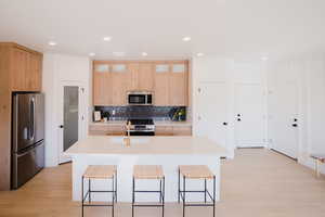 Model Home PicsKitchen with light wood-type flooring, stainless steel appliances, a sink, and a kitchen bar