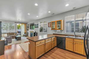 Kitchen featuring a peninsula, a sink, dark countertops, black dishwasher, and wood finished floors