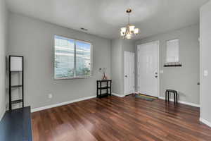 Foyer with wood finished floors, visible vents, baseboards, and an inviting chandelier