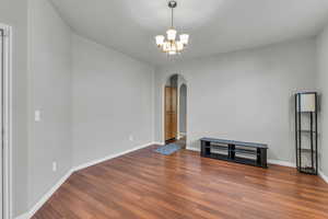 Empty room with wood finished floors, arched walkways, and a notable chandelier