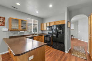 Kitchen featuring dark countertops, a sink, black appliances, a peninsula, and dark wood-type flooring