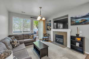 Carpeted living room with a tiled fireplace, visible vents, and baseboards