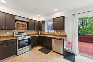 Kitchen with stainless steel appliances, a sink, tasteful backsplash, open shelves, and light tile patterned floors