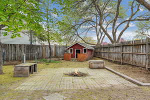 View of patio with a fenced backyard, an outdoor structure, a storage shed, and an outdoor fire pit